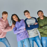 four cheerful men in casual outfits smiling at camera posing on grey backdrop, cultural diversity
