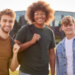 portrait of three male university or college student standing outdoors by modern campus building