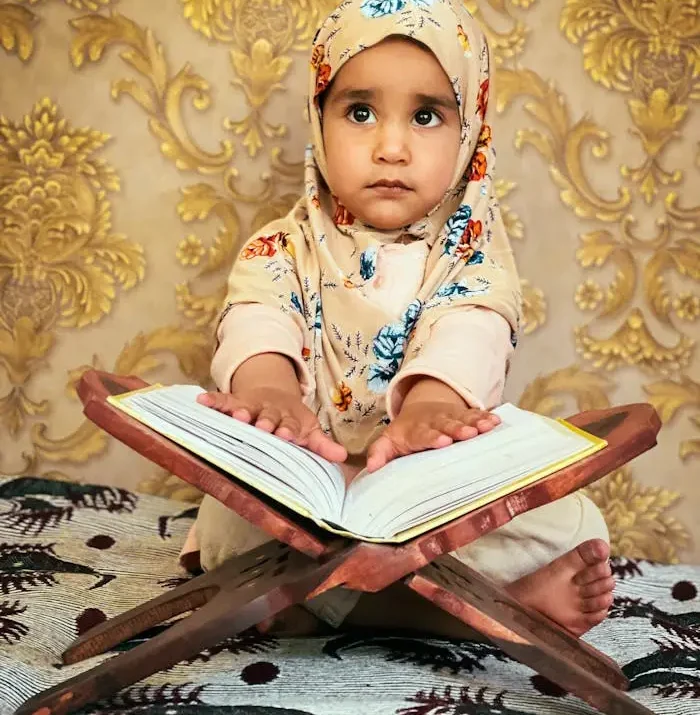 Little girl in hijab reading Quran indoors, embracing Islamic culture.