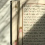 An open Quran on a table with shadows, reflecting a serene and contemplative atmosphere.